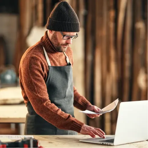 Handwerker vergleicht Gewerbestrom-Tarife am Laptop in der Werkstatt