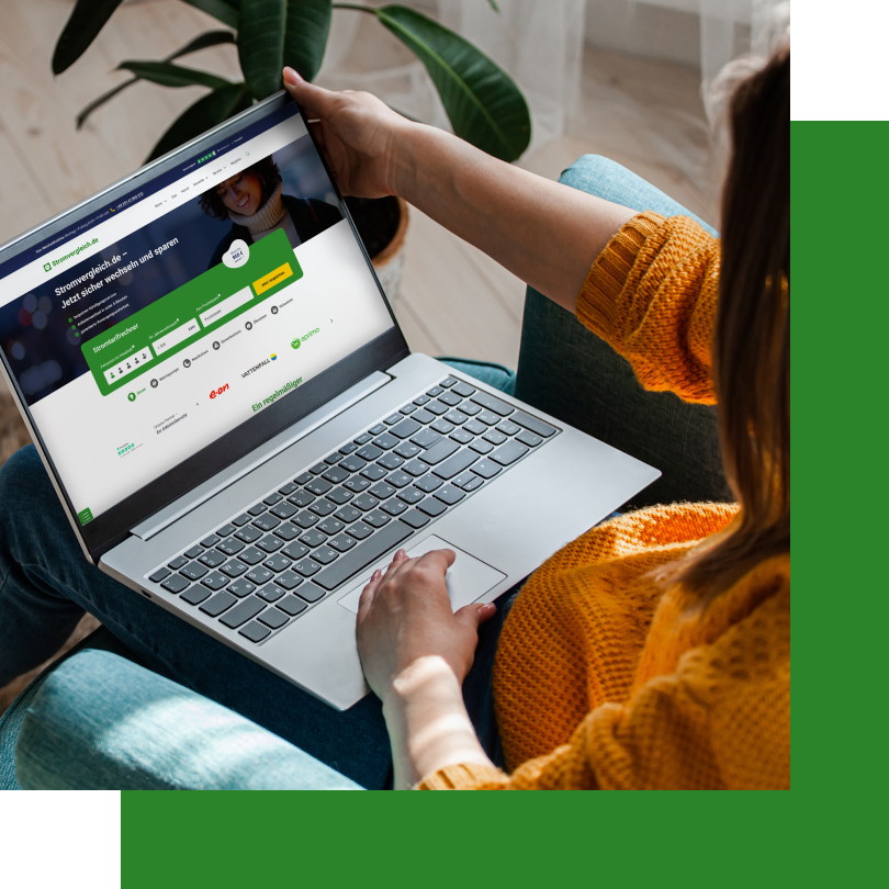 Eine Frau sitzt entspannt in einem Sessel und hält einen Laptop auf ihrem Schoß. Auf dem Bildschirm ist die Website von Stromvergleich.de geöffnet, auf der ein Stromtarifvergleich zu sehen ist. Sie trägt einen gelben Strickpullover, und im Hintergrund sind eine grüne Zimmerpflanze sowie ein heller Raum mit Vorhängen zu erkennen.