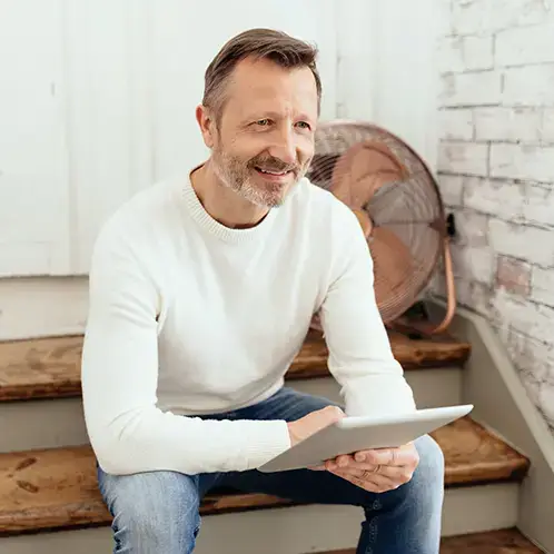 Wie oft sollte man den Stromanbieter wechseln? Ein lächelnder Mann mit sitzt entspannt auf einer Holztreppe und hält ein Tablet in den Händen.